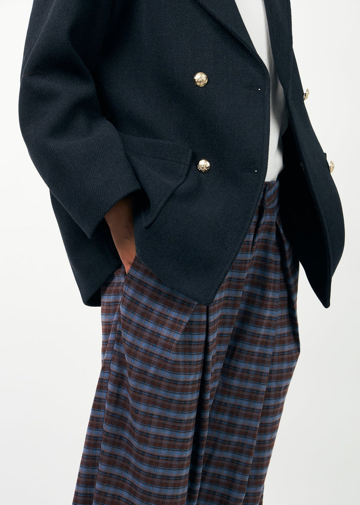 Person wearing a dark navy blazer with gold buttons and plaid pants on a white background