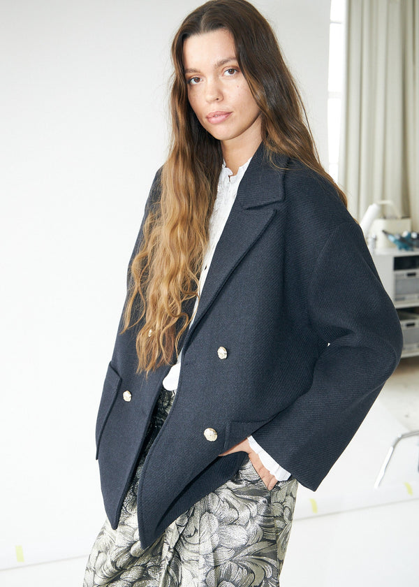 Woman wearing a navy blue coat with white buttons indoors.