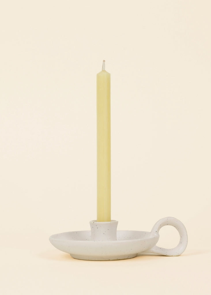 Ceramic candle holder with a lit candle on a beige background