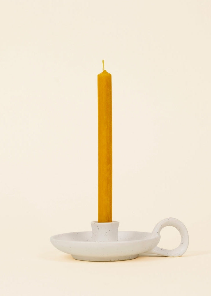 Yellow candle in a white ceramic holder on a beige background