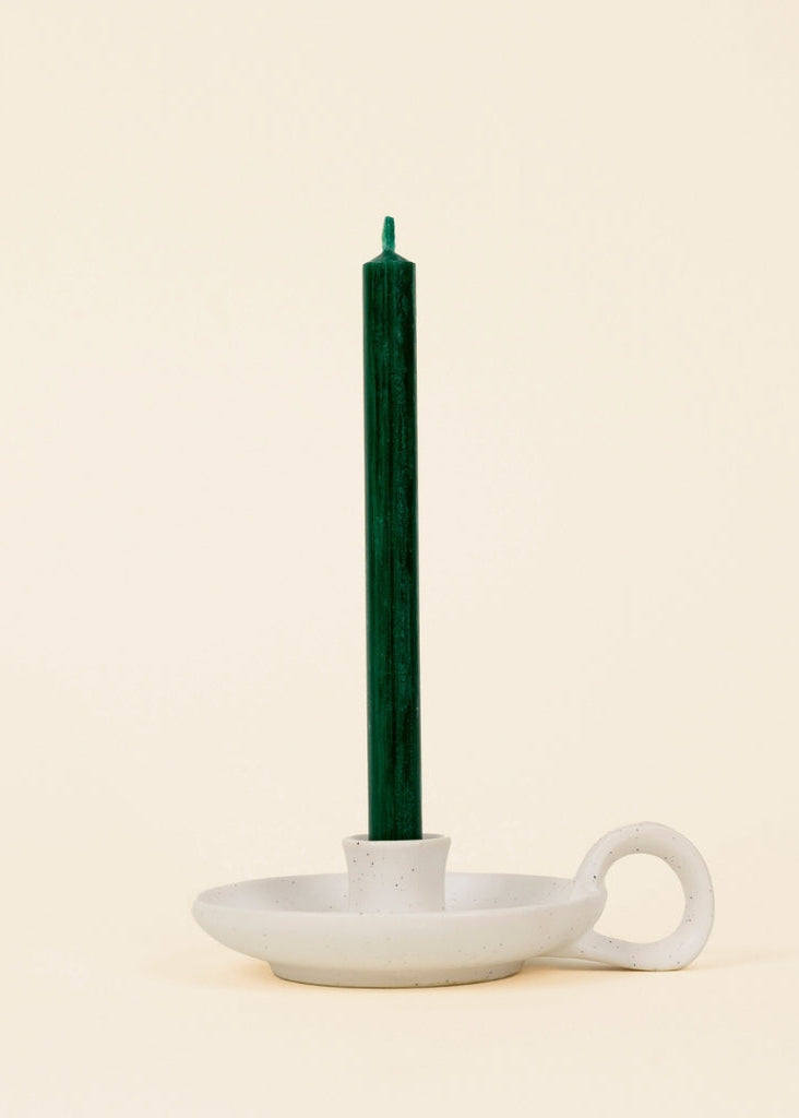 Green candle in a white ceramic holder on a beige background
