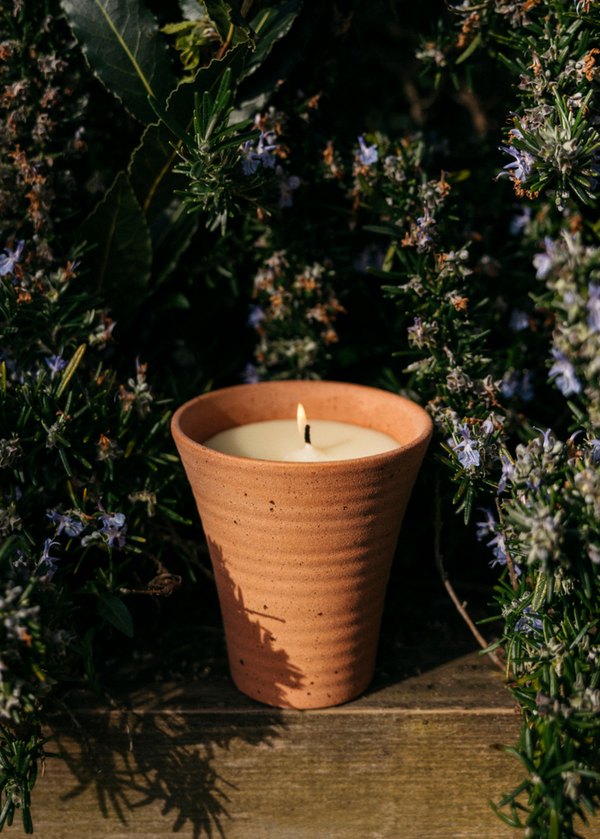 Terracotta candle holder with a lit candle surrounded by greenery on a wooden surface