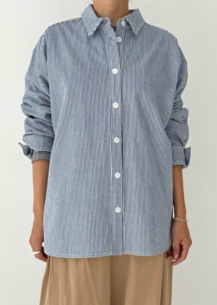 Person wearing a blue and white striped shirt with rolled-up sleeves on a plain background