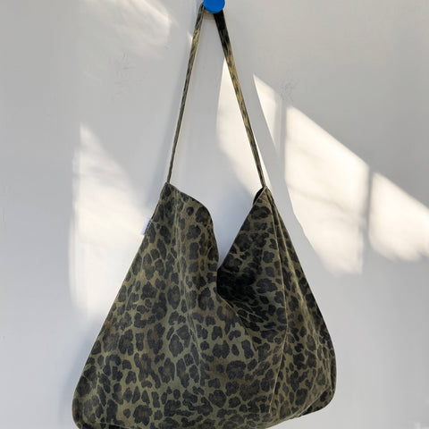 Leopard print bag hanging on a white wall with a blue tape measure next to it.
