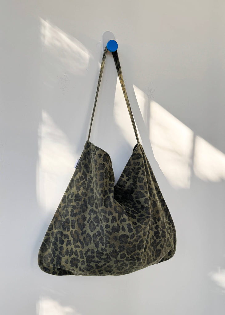 Leopard print bag hanging on a white wall with a blue tape measure next to it.