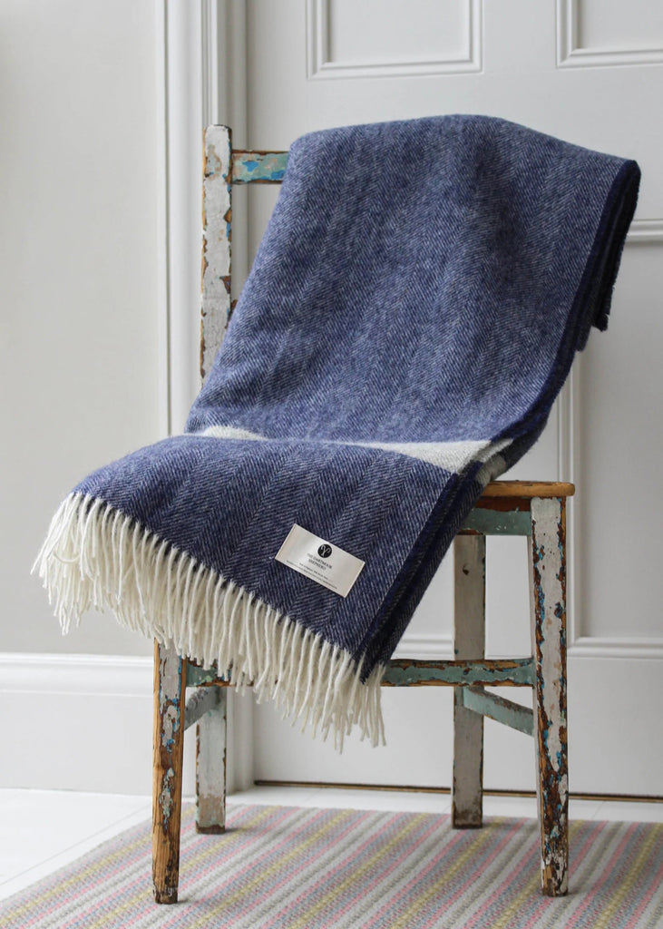 Blue blanket with fringes draped over a wooden chair against a white wall.