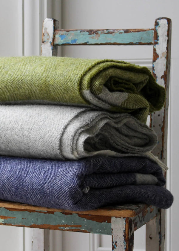 Stack of folded blankets in green, gray, and blue on a rustic wooden chair.