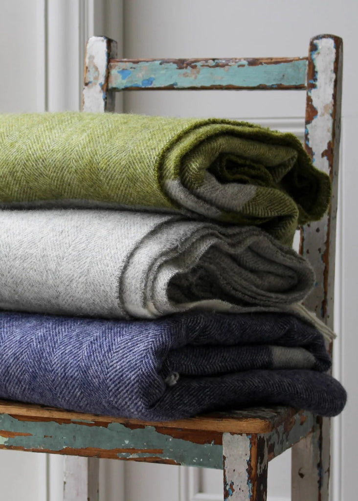 Stack of folded blankets in green, gray, and blue on a rustic wooden chair.