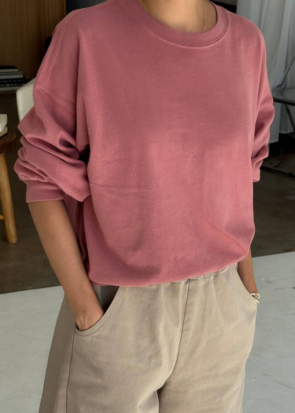 Person wearing a pink sweatshirt and beige pants indoors.