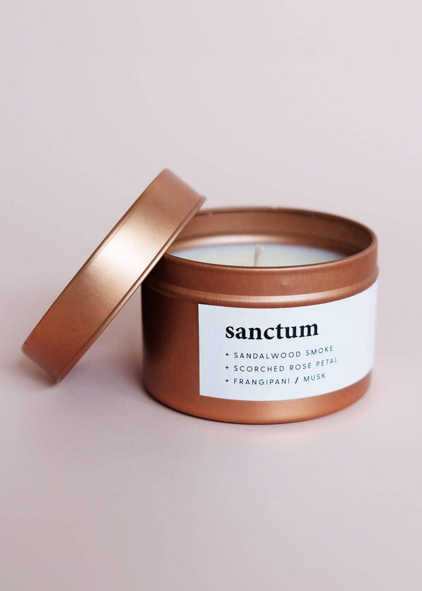 Candle in a bronze tin with 'sanctum' label on a light pink background