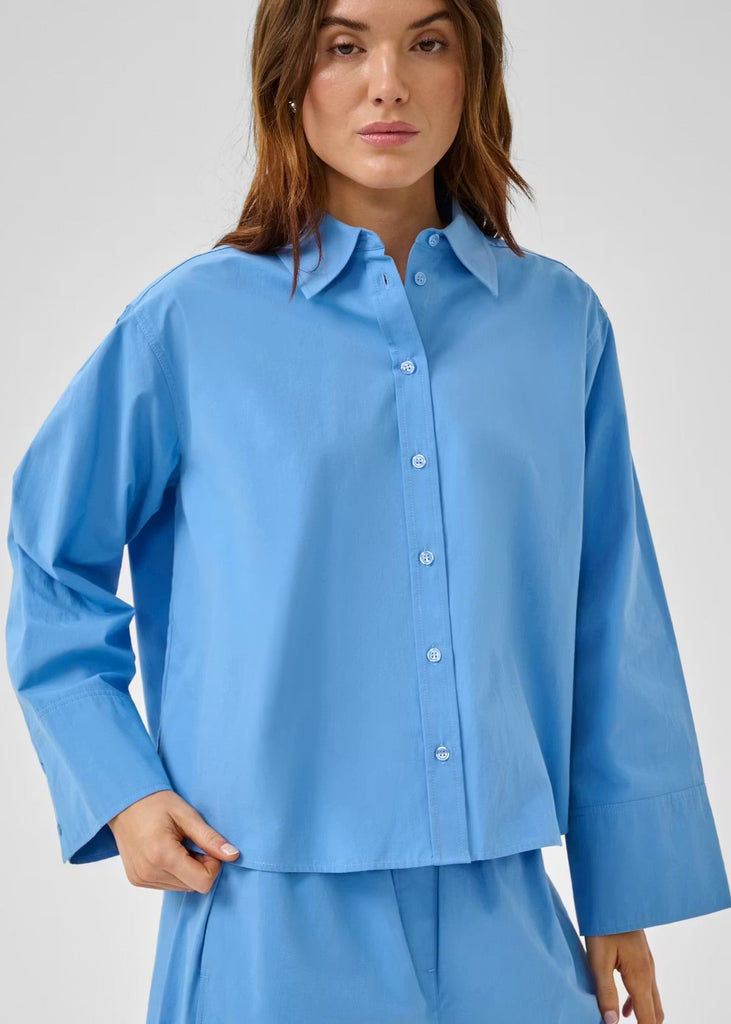 Woman wearing a blue shirt and pants set against a plain background