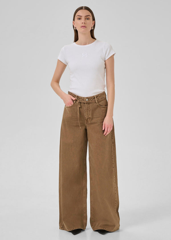 Woman wearing brown wide-leg pants and a white t-shirt on a light gray background