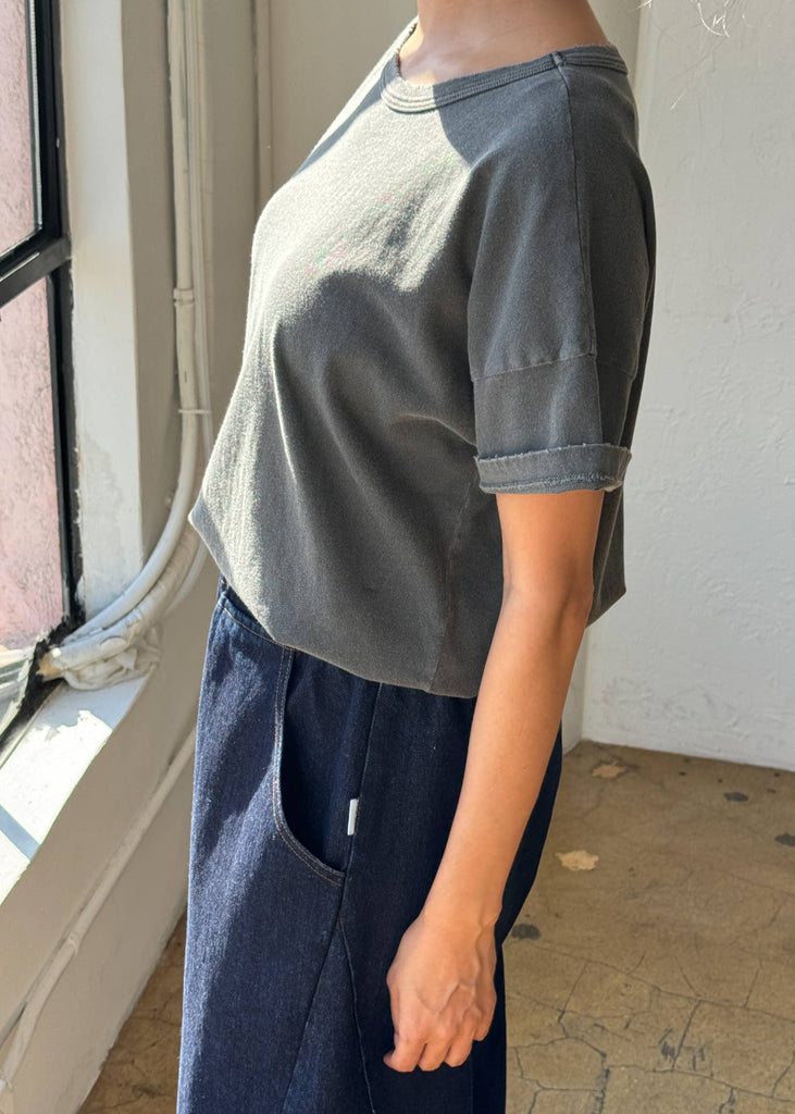 Person wearing a gray t-shirt and navy pants standing indoors near a window.