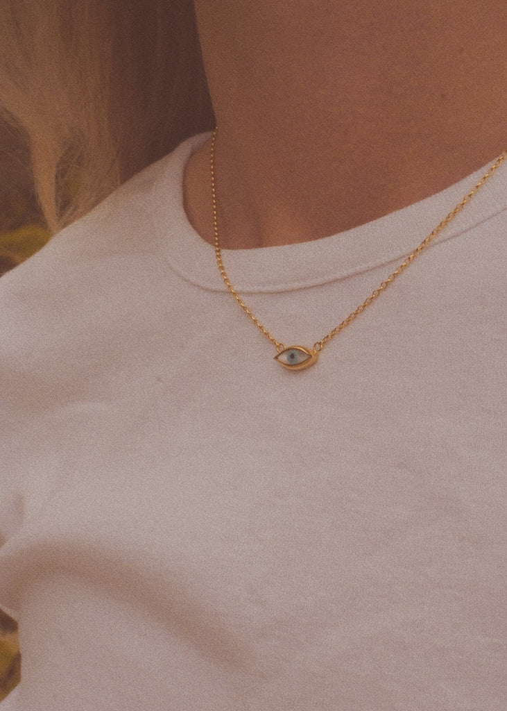 Gold necklace with a small pendant worn by a person against a neutral background