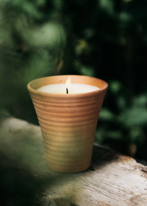 Candle in a terracotta holder on a wooden surface with a blurred green background