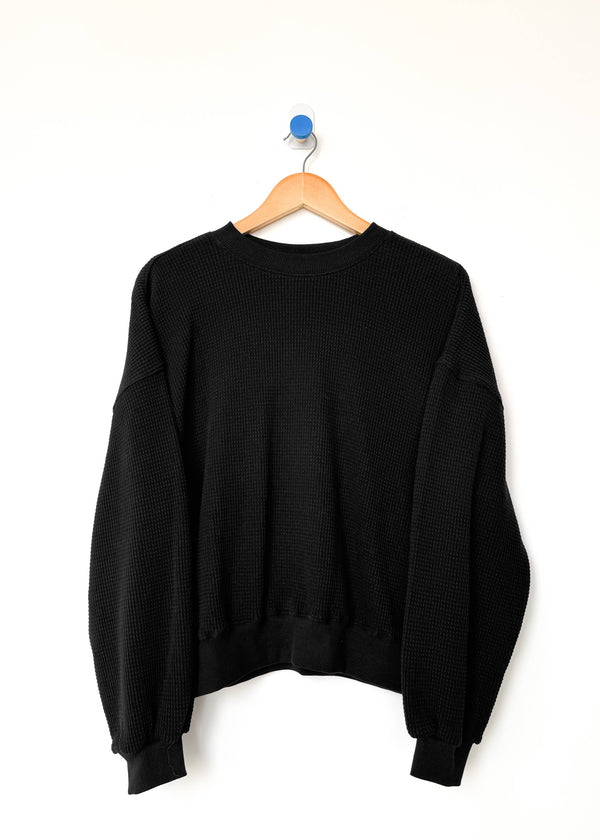 Black sweater on a wooden hanger against a white background