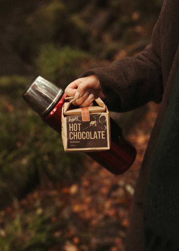 Person holding a container of hot chocolate in a forest setting