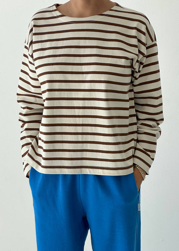 Person wearing a brown and white striped shirt with blue pants on a white background