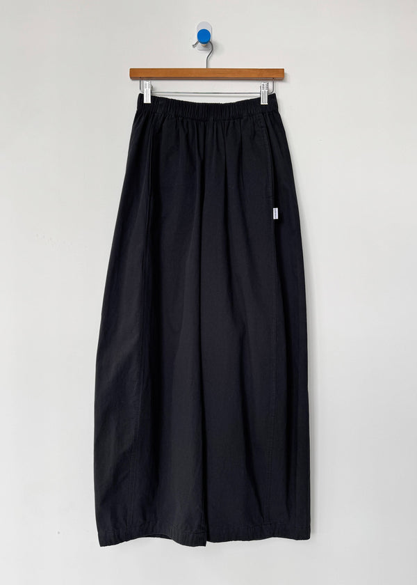 Black pants hanging on a wooden hanger against a white wall