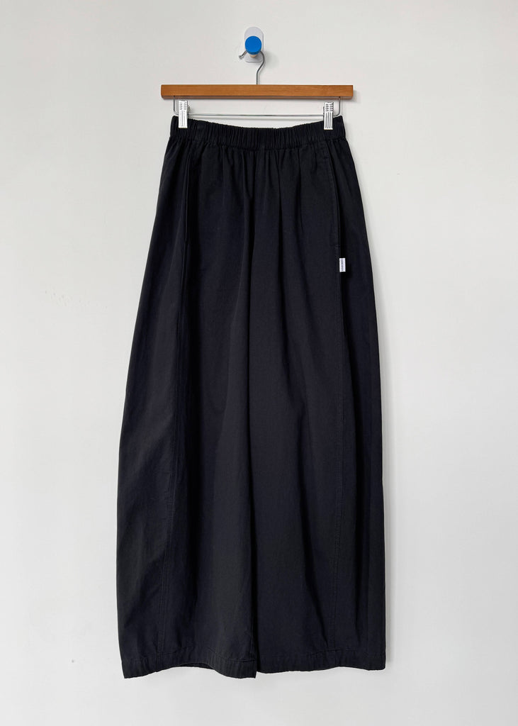 Black pants hanging on a wooden hanger against a white wall