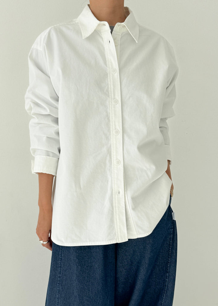 Person wearing a white button-up shirt and blue jeans against a plain background