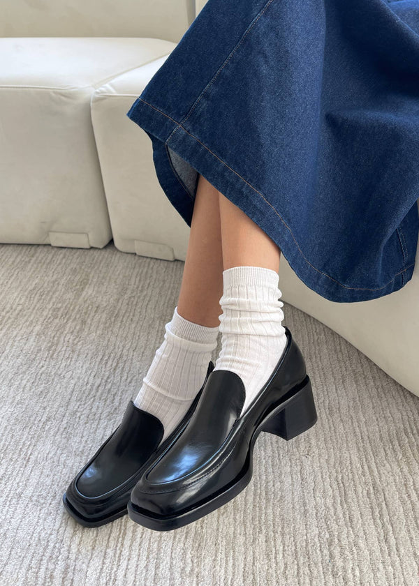 Person wearing black shoes, white socks, and blue jeans on a carpeted floor.