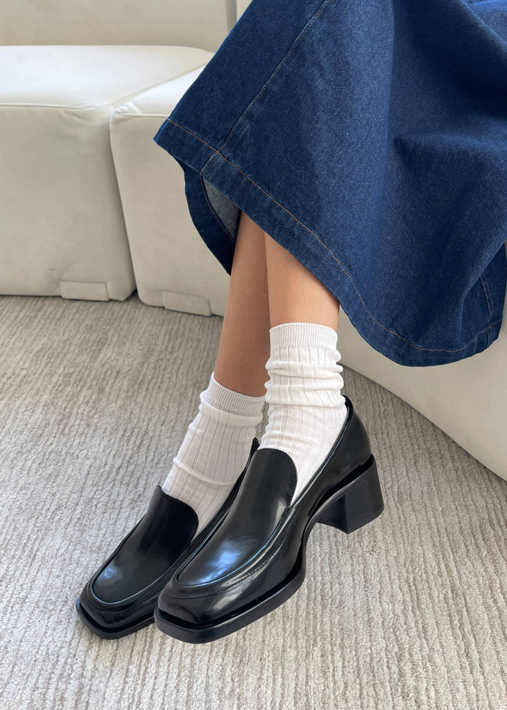 Person wearing black shoes, white socks, and blue jeans on a carpeted floor.