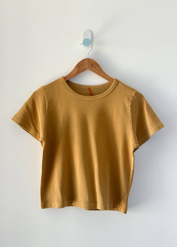 Mustard yellow t-shirt on a wooden hanger against a white background