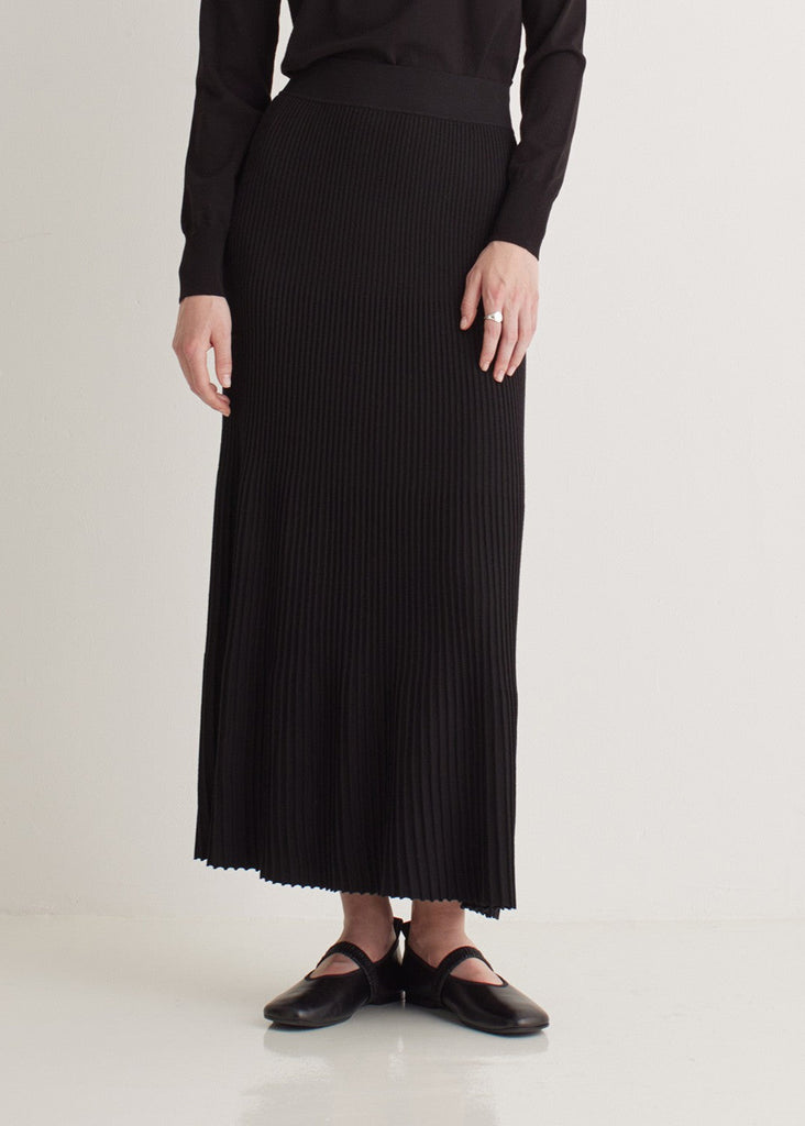 Person wearing a black ribbed skirt and black shoes on a white background