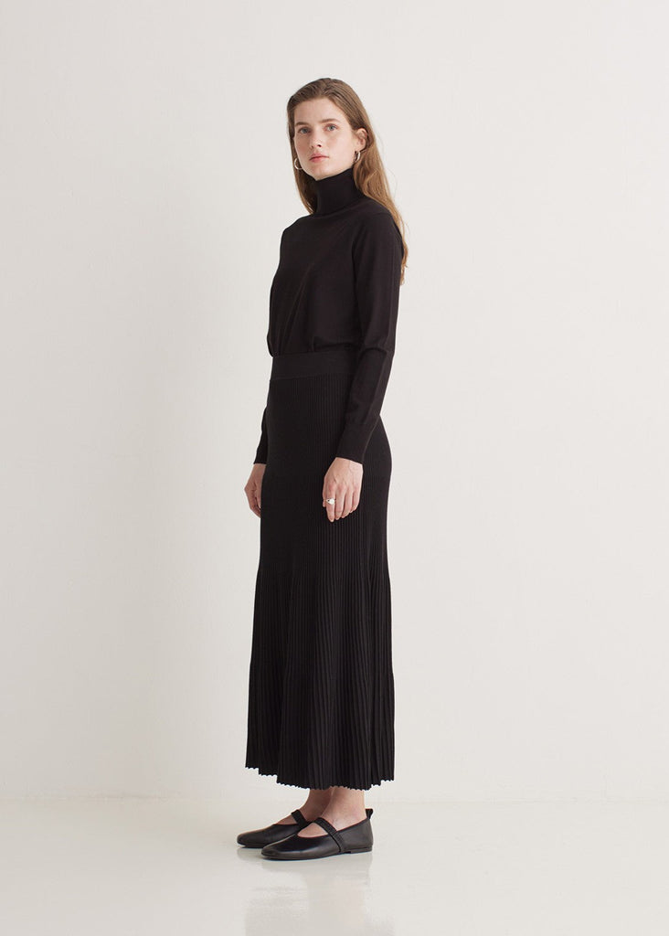 Woman wearing a black turtleneck and pleated skirt on a white background