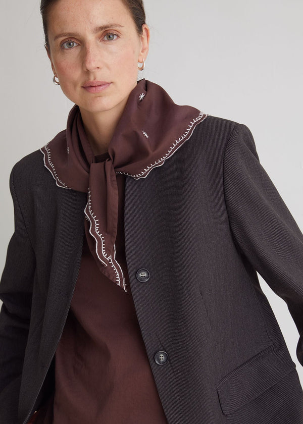 Woman wearing a dark blazer and brown scarf against a plain background