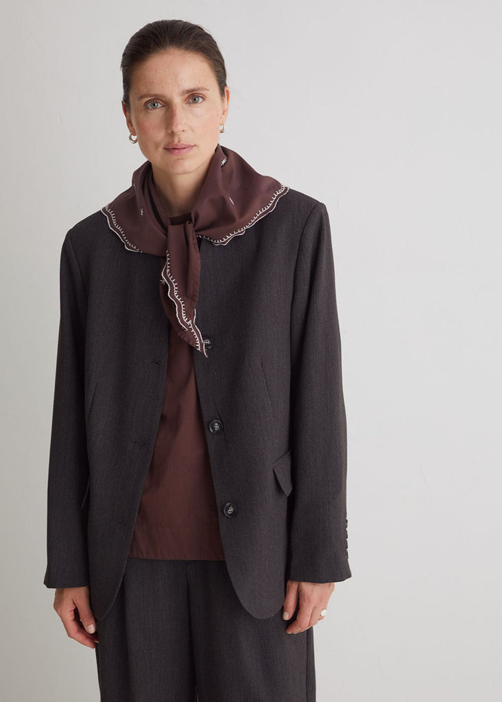 Woman wearing a dark coat with a matching scarf against a plain background