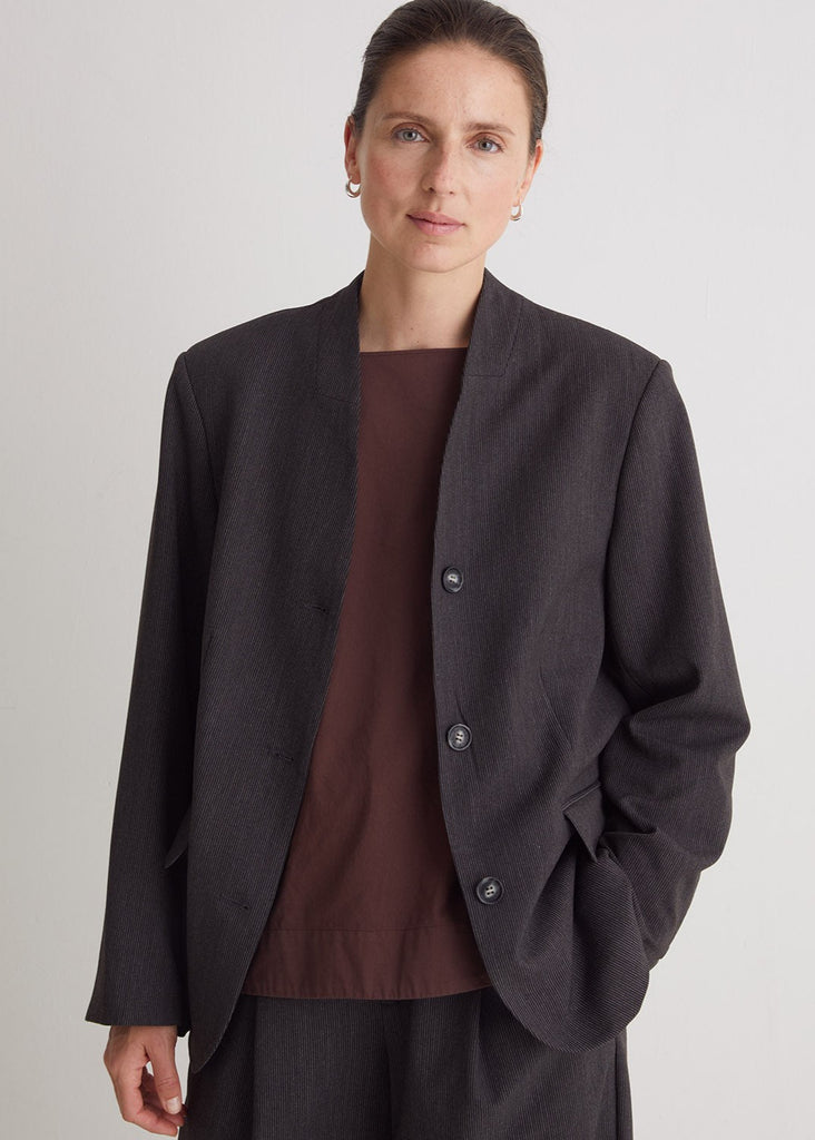Woman wearing a dark gray blazer over a brown top on a light gray background