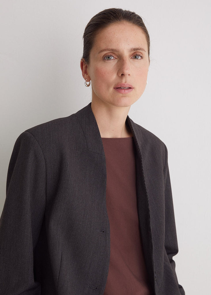 Woman wearing a dark gray coat over a brown top against a plain background