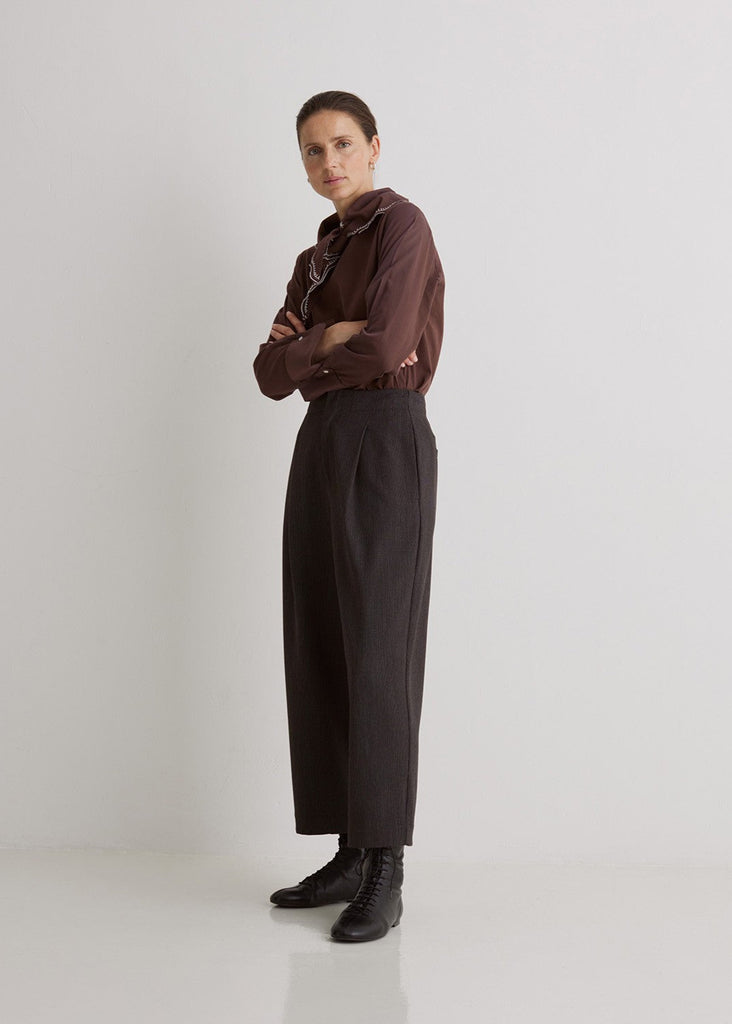 Person wearing a brown shirt and black pants on a white background