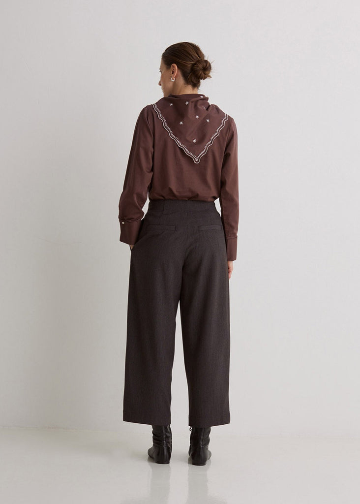 Person wearing a brown blouse with lace details and dark pants on a white background