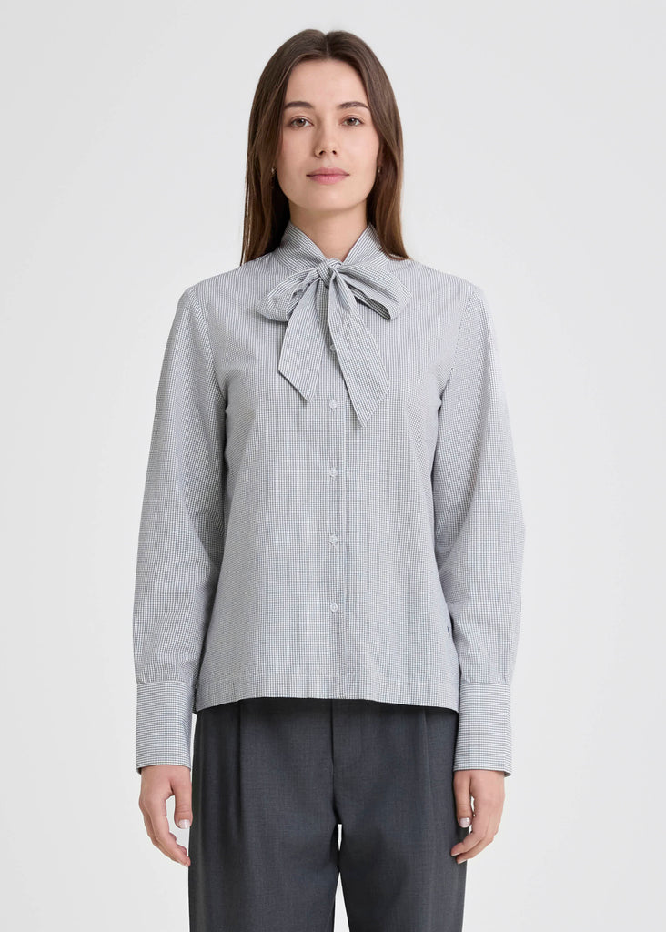 Woman wearing a light gray blouse with a tie collar on a white background