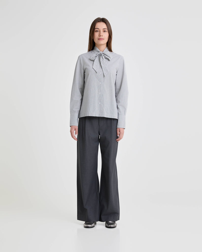 Person wearing a light gray checkered blouse with a bow and dark gray wide-leg pants on a white background
