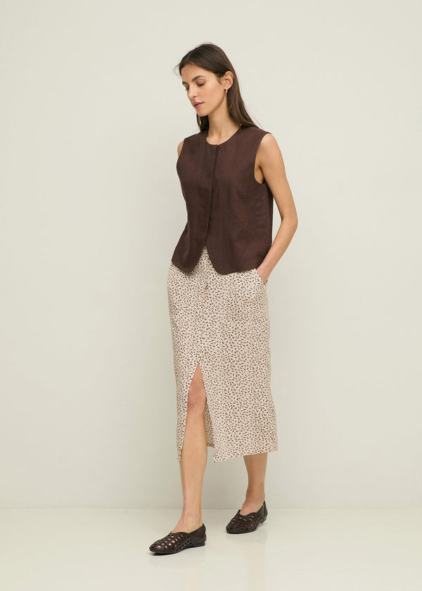 Woman wearing a brown sleeveless top and patterned skirt on a white background