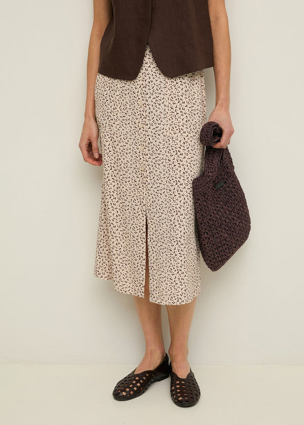 Person wearing a patterned skirt and brown top, holding a matching bag against a plain background