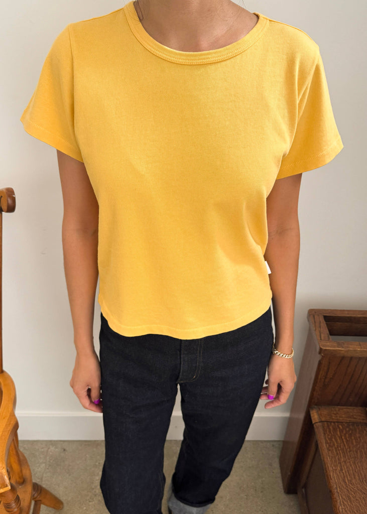 Person wearing a yellow t-shirt and dark pants standing indoors.