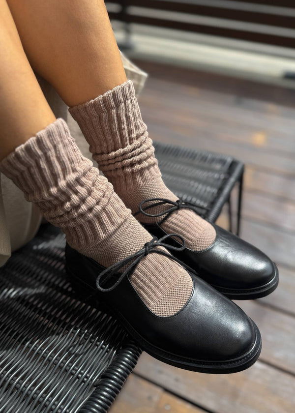 Person wearing beige ribbed socks and black shoes on a wooden floor.