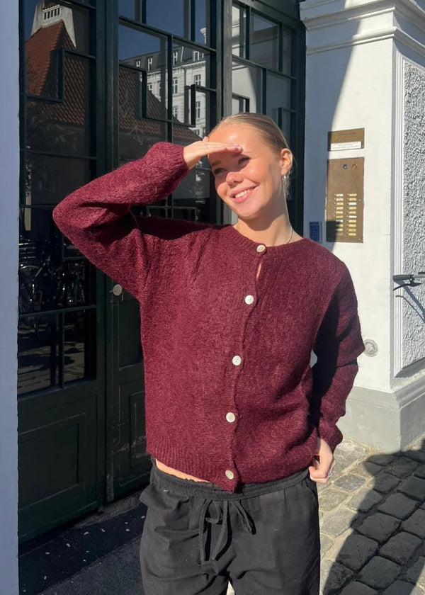 Person wearing a maroon cardigan with white buttons outdoors.