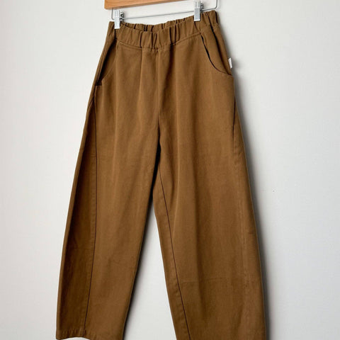 Brown pants hanging on a wooden hanger against a white background