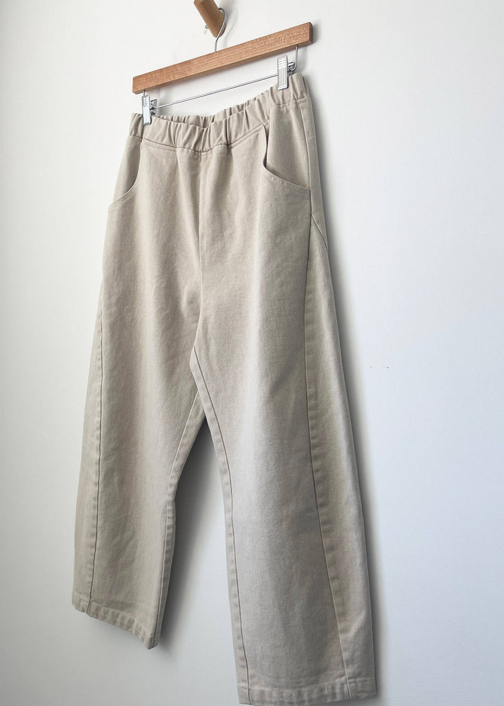 Beige pants hanging on a wooden hanger against a white wall