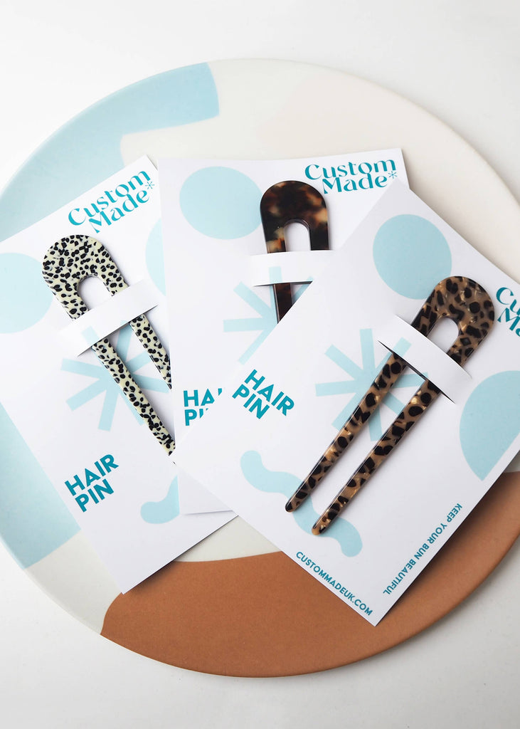Leopard print hair pins on 'Custom Made' branded cards with a round wooden board background.