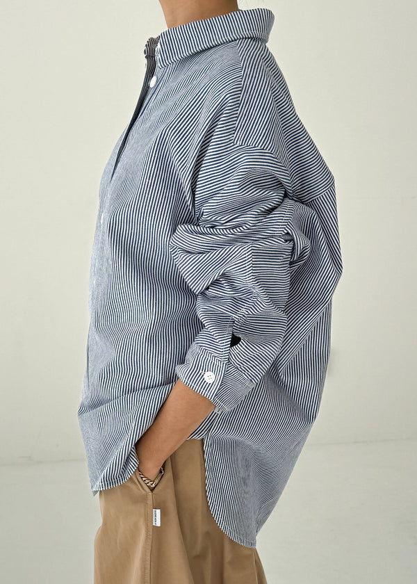 Person wearing a blue and white striped shirt with rolled-up sleeves on a plain background