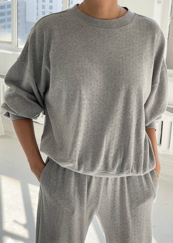 Person wearing a gray oversized sweatshirt and pants in a bright room.