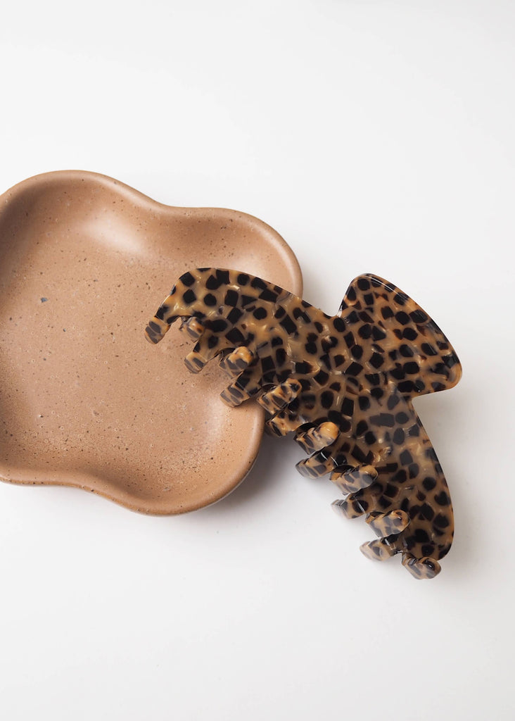 Leopard print hair clip on a beige ceramic dish against a white background