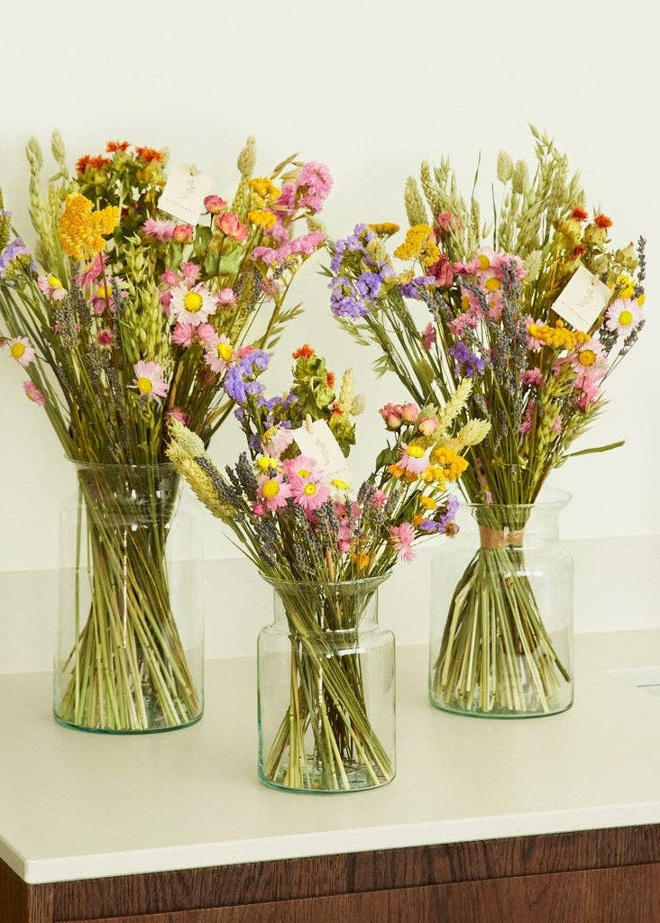 Three glass vases filled with colorful dried flowers on a white surface.